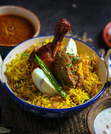 A delicious Indian chicken biryani with eggs, garnished with chilies, served with curry sauce and raita.